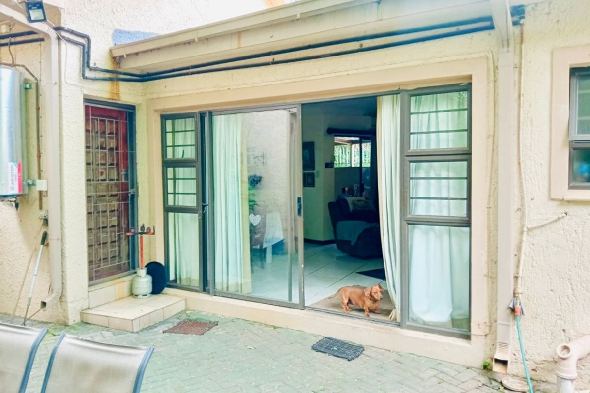 Rear exterior view showing a paved patio area, sliding glass door access, and external utility fixtures including a geyser and drainage system.