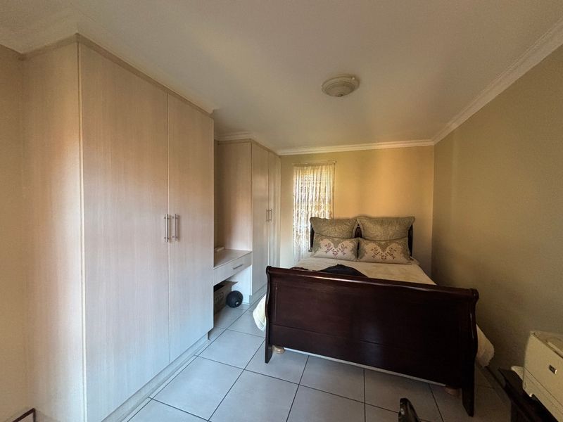 A bedroom featuring light-toned built-in cupboards with an integrated vanity, tiled flooring, and coved ceiling details.