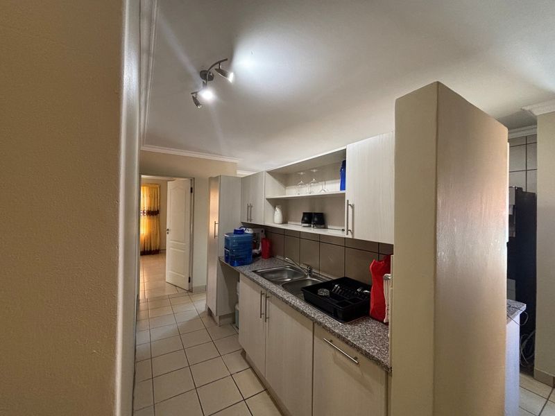A functional kitchen area featuring built-in cabinetry, granite countertops, and a double basin sink, with tiled flooring and modern spotlight lighting.