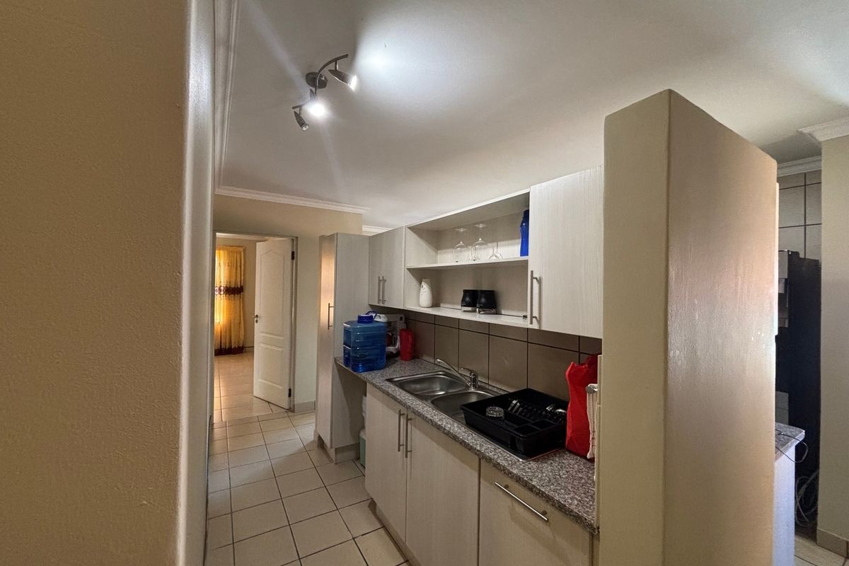 A functional kitchen area featuring built-in cabinetry, granite countertops, and a double basin sink, with tiled flooring and modern spotlight lighting.