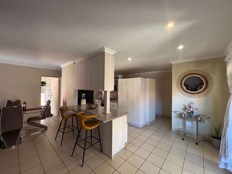 Open-plan kitchen and dining area featuring a granite-topped island, tiled flooring, and recessed lighting, creating a functional and connected living space.