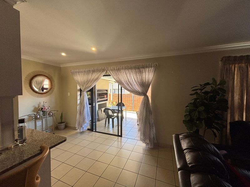 Open-plan living area featuring tiled floors and sliding glass doors leading to a covered patio with a built-in braai.