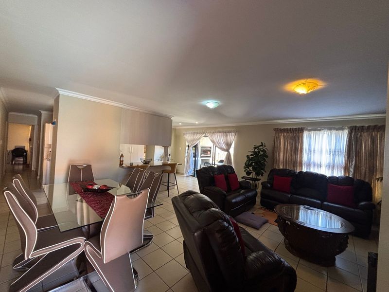 Spacious open-plan living and dining area featuring ceramic floor tiles, a breakfast bar, and direct access to the patio through sliding glass doors.