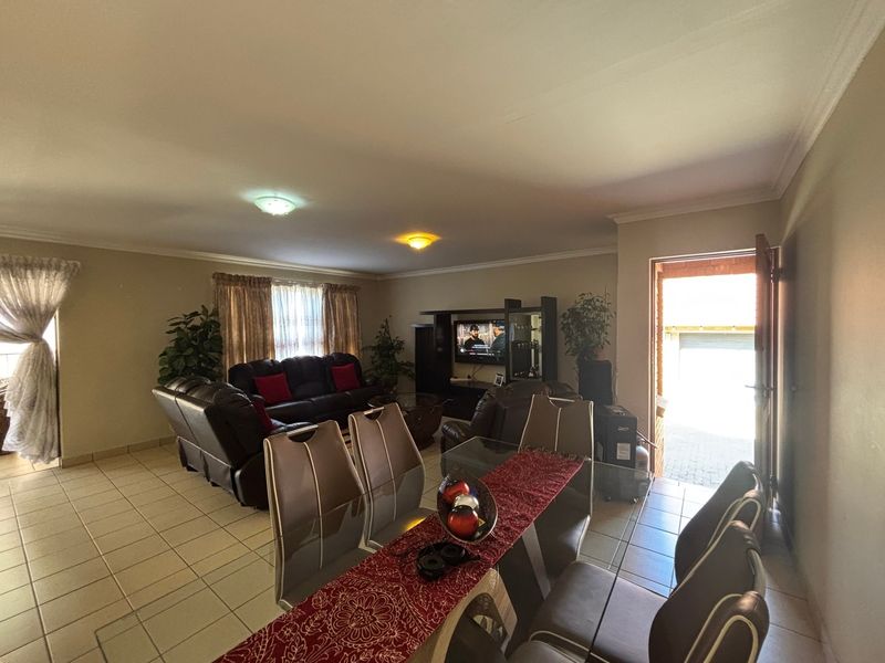 Spacious open-plan living and dining area featuring neutral tiled flooring, cove cornicing, and direct access to the exterior.