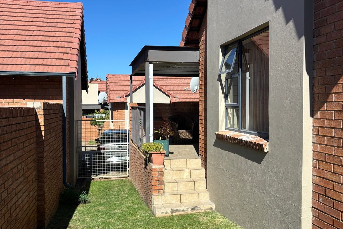 Rear exterior view of the townhouse featuring a small garden, a covered patio with tiled steps, and brick boundary walls.