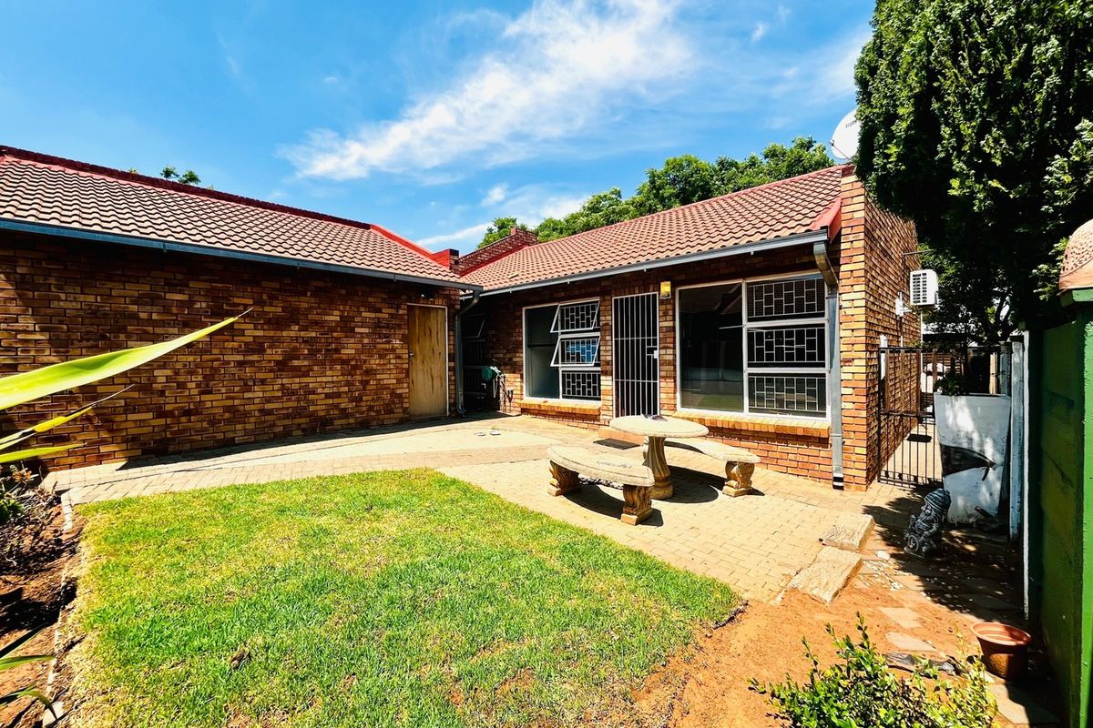 A rear exterior view of a face brick townhouse featuring a paved patio area, lawn, and secure window fittings.
