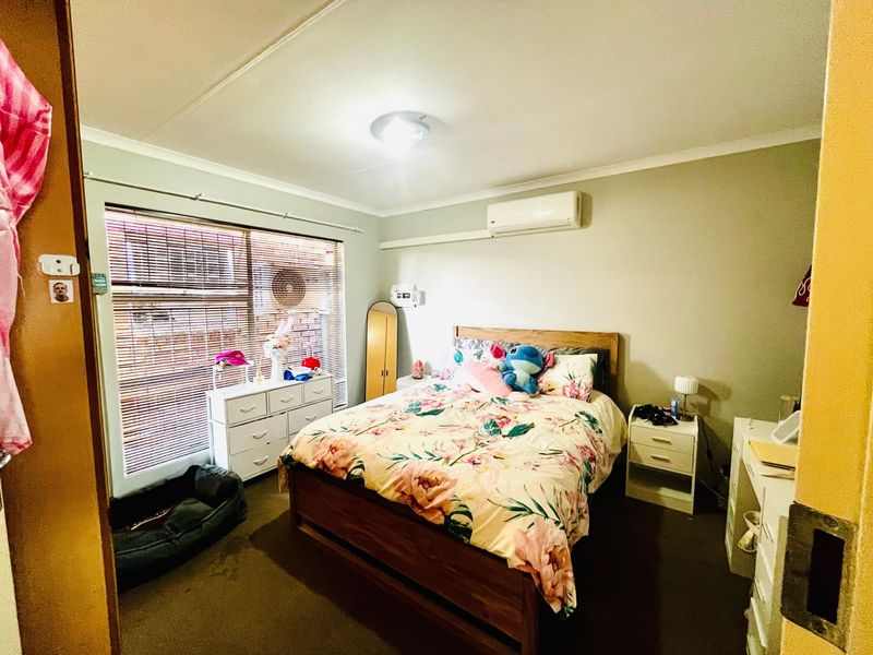 A functional bedroom featuring a wall-mounted split-system air conditioner, venetian blinds, and neutral wall finishes.