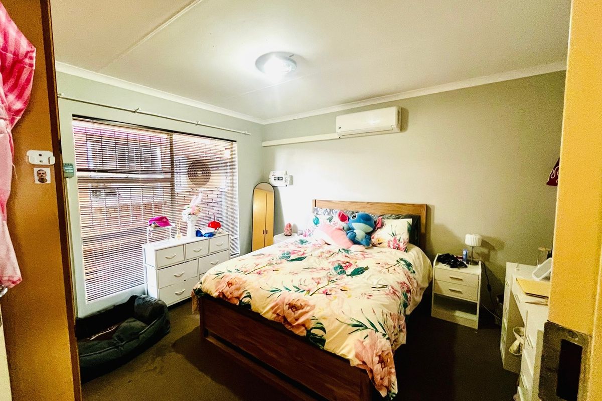 A functional bedroom featuring a wall-mounted split-system air conditioner, venetian blinds, and neutral wall finishes.