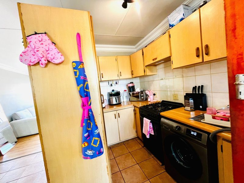 A functional kitchen featuring wooden cabinetry, tiled backsplash, gas stove, and tiled flooring, offering a practical layout for daily cooking and laundry needs.