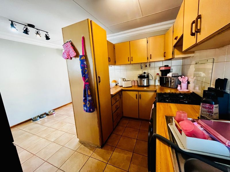 A functional kitchen featuring dated cabinetry, laminate countertops, a gas hob, and tiled flooring, offering potential for a modern renovation.