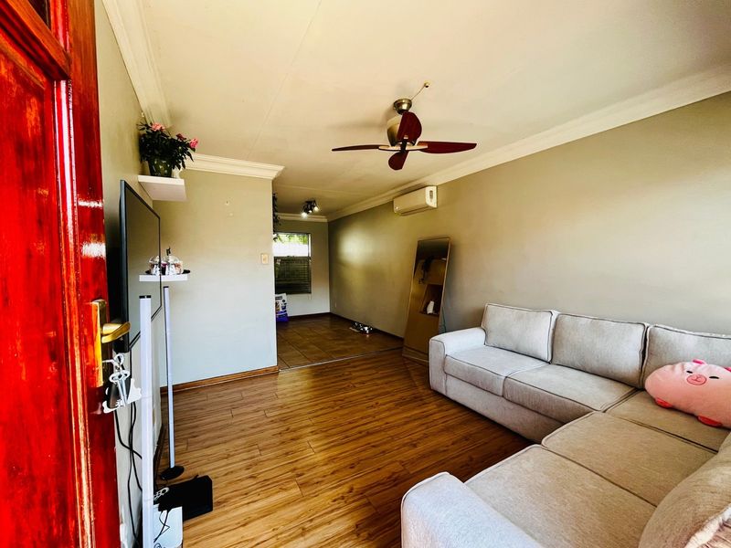 A living room featuring laminate flooring, crown molding, a ceiling fan, and a wall-mounted air conditioning unit.