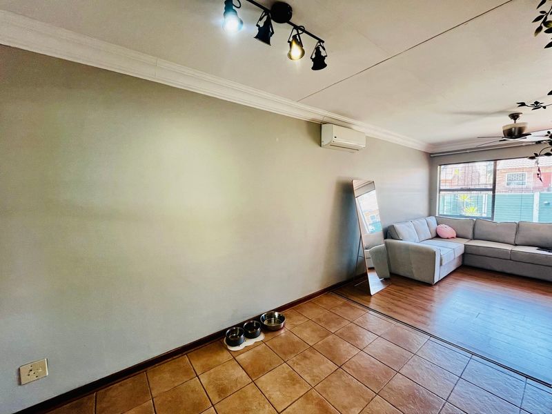 A living room featuring a mix of tiled and laminate flooring, equipped with a split-system air conditioner, ceiling fan, and track lighting.
