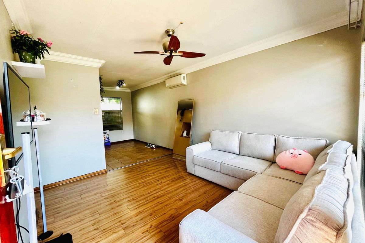 Spacious living area featuring laminate flooring, crown molding, a ceiling fan, and a wall-mounted air conditioning unit, leading into an adjacent tiled space.