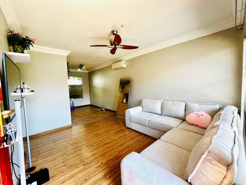 Spacious living area featuring laminate flooring, crown molding, a ceiling fan, and a wall-mounted air conditioning unit, leading into an adjacent tiled space.