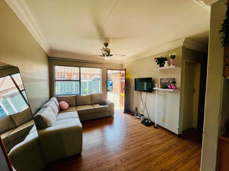 A comfortable living room featuring laminate flooring, a ceiling fan, and direct access to the exterior through a security gate.