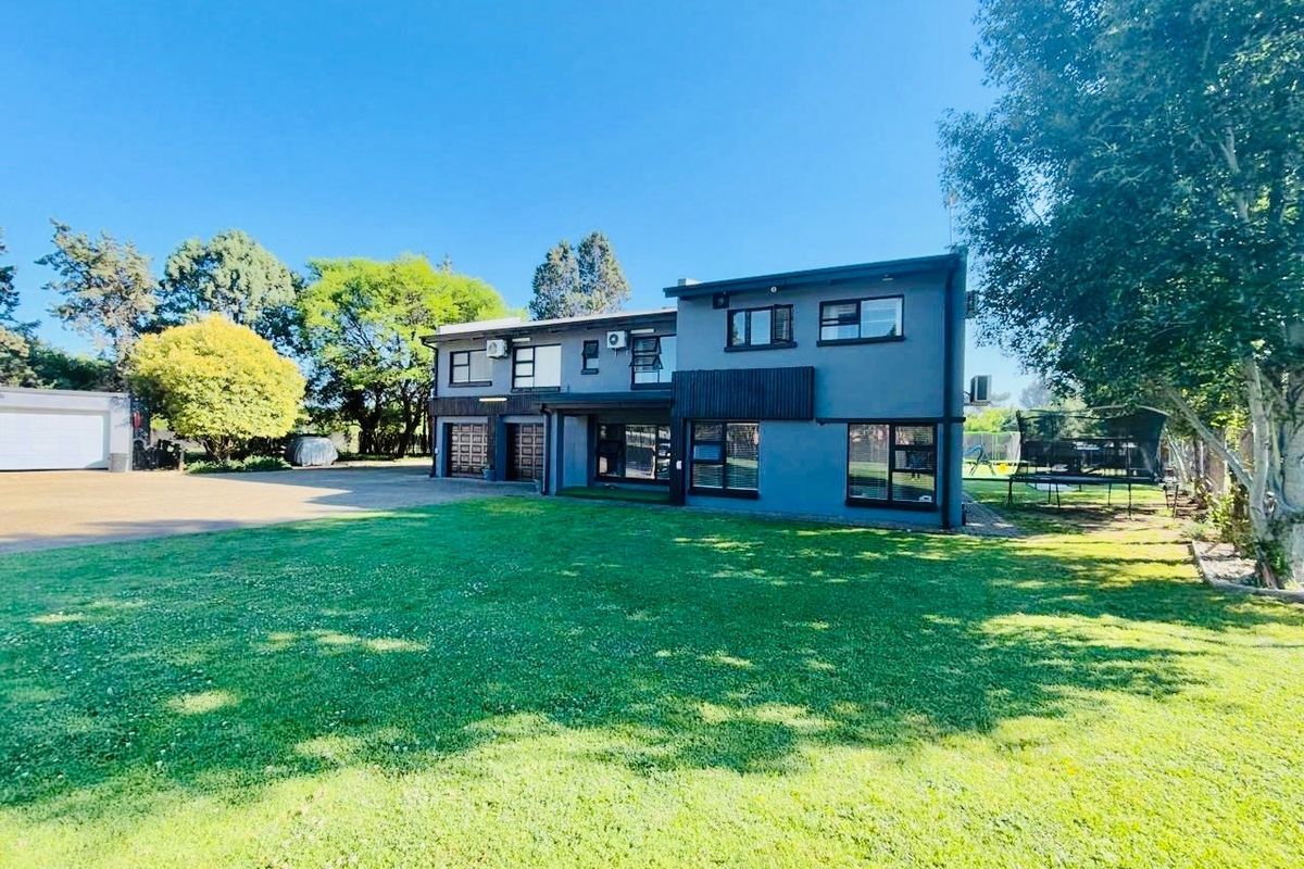 A spacious rear view of a double-storey property featuring a large manicured lawn, paved driveway, and modern dark-framed windows.