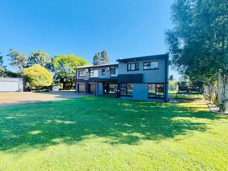 A spacious rear view of a double-storey property featuring a large manicured lawn, paved driveway, and modern dark-framed windows.