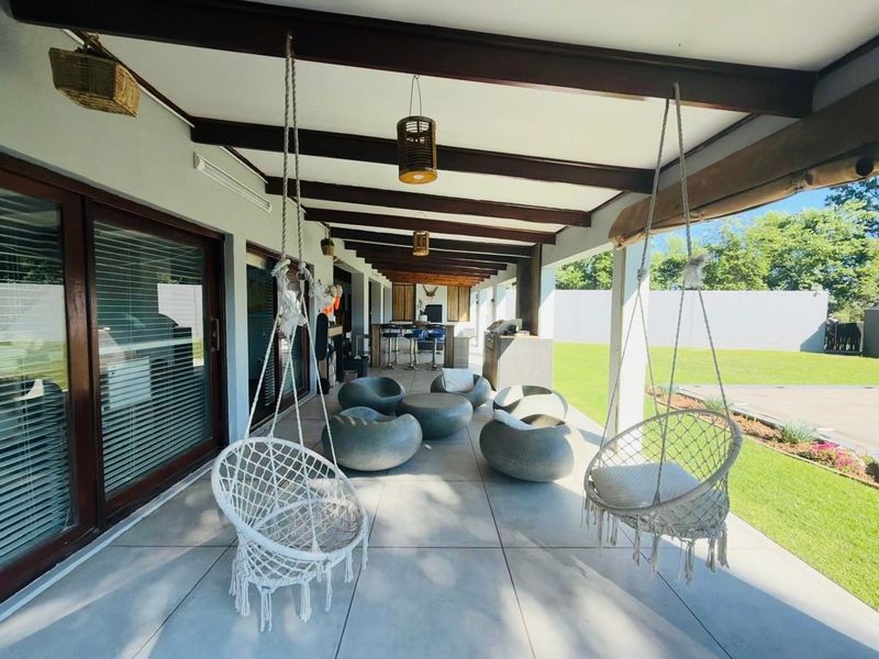 Spacious covered patio featuring exposed timber beams, tiled flooring, and a built-in outdoor bar area, perfect for entertaining overlooking the garden.