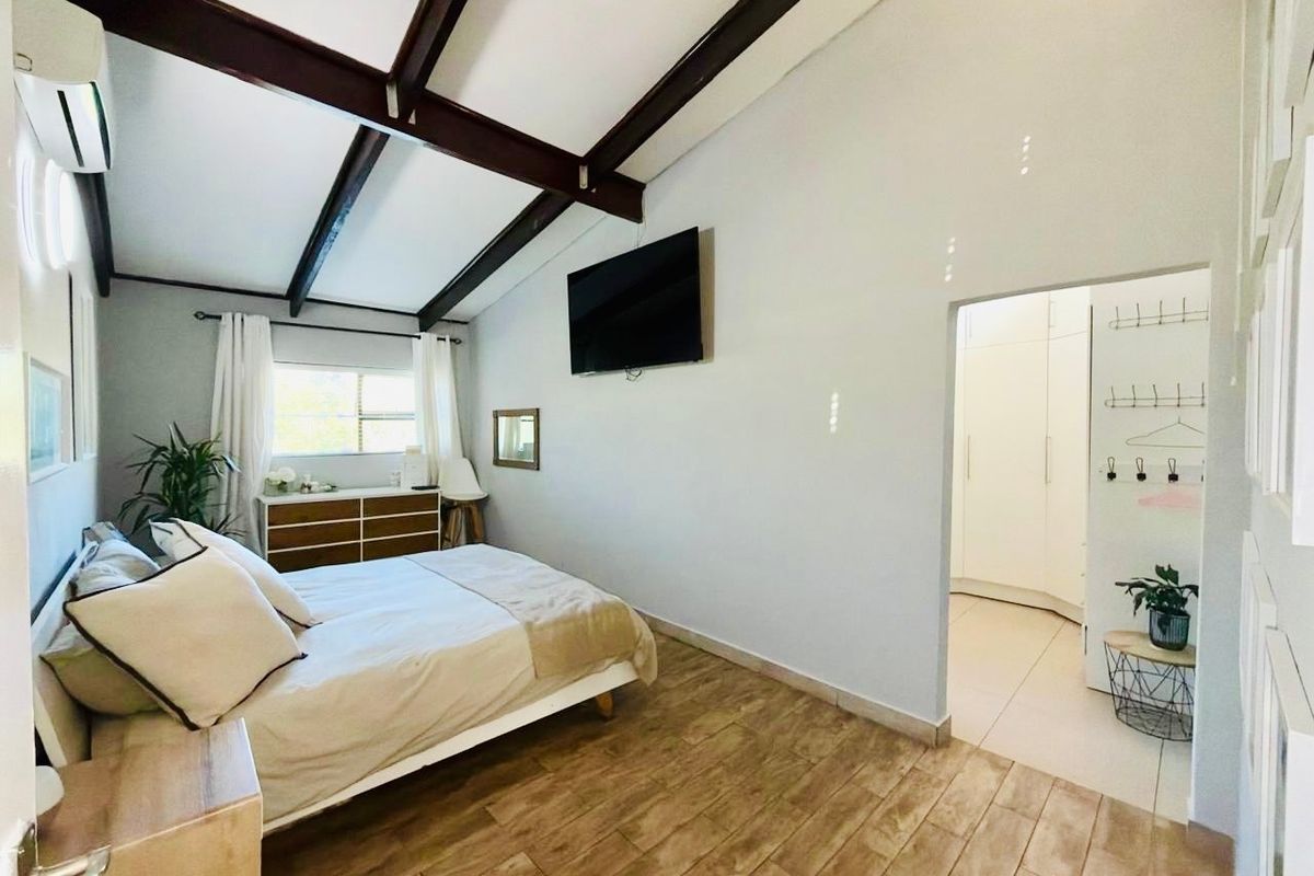 Spacious bedroom featuring exposed timber ceiling beams, tiled flooring, an air conditioning unit, and an adjoining walk-in closet area with built-in cupboards.