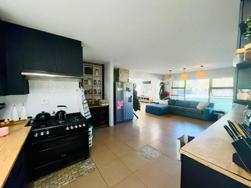 Spacious open-plan living area featuring a modern kitchen with dark cabinetry, gas stove, and tiled flooring, seamlessly flowing into the adjacent lounge space.