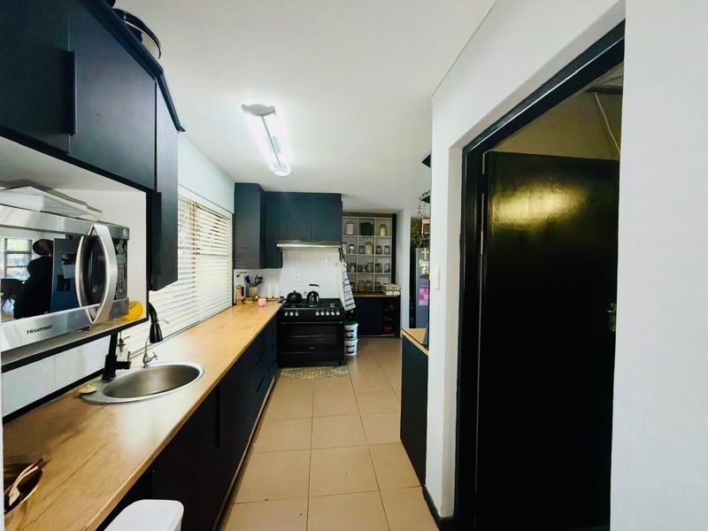 A modern galley-style kitchen featuring dark cabinetry, wooden countertops, a gas stove with extractor fan, and tiled flooring.