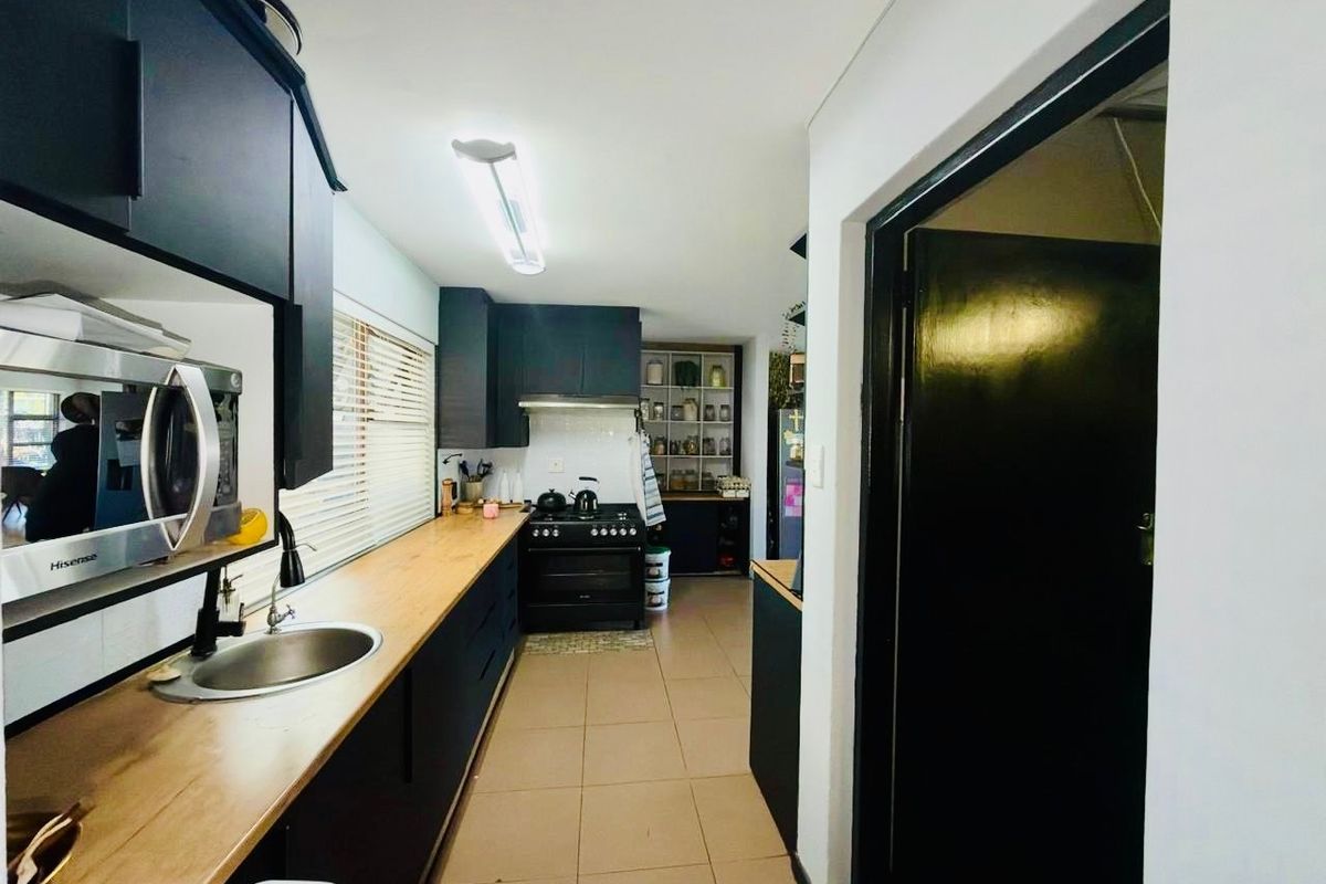 A modern galley-style kitchen featuring dark cabinetry, wooden countertops, a gas stove with extractor fan, and tiled flooring.