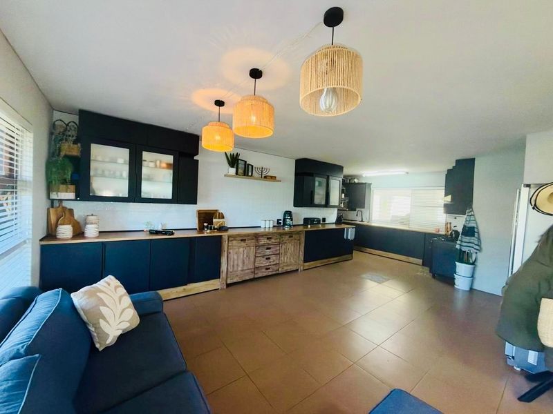 Spacious open-plan kitchen and living area featuring modern dark cabinetry, wooden countertops, tiled flooring, and stylish pendant lighting.
