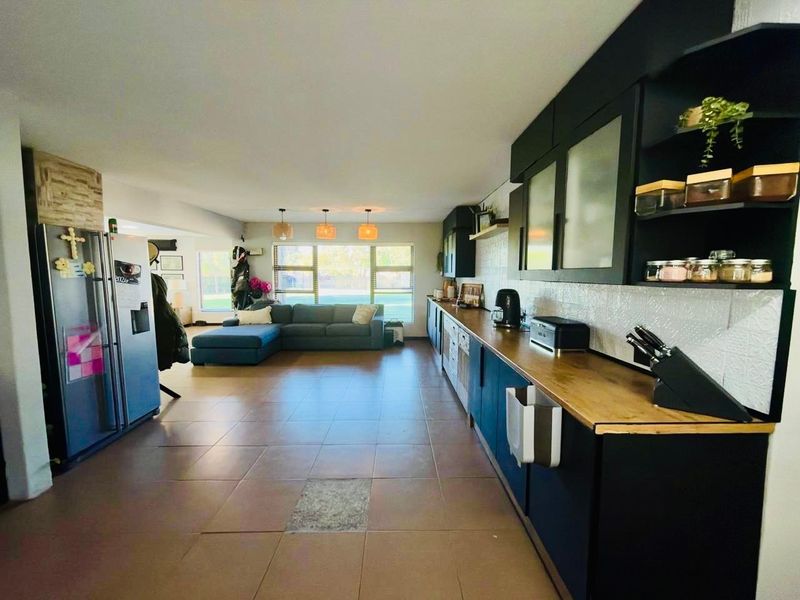 Spacious open-plan living area featuring a modern kitchen with dark cabinetry, wooden countertops, and tiled flooring, seamlessly flowing into the lounge space.