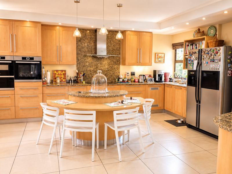 Spacious kitchen featuring light wood cabinetry, granite countertops, integrated double ovens, and a central circular breakfast nook with tiled flooring throughout.