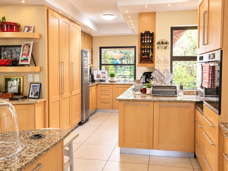 A well-maintained kitchen featuring light wood cabinetry, granite countertops, built-in oven, and tiled flooring with ample natural light from large windows.