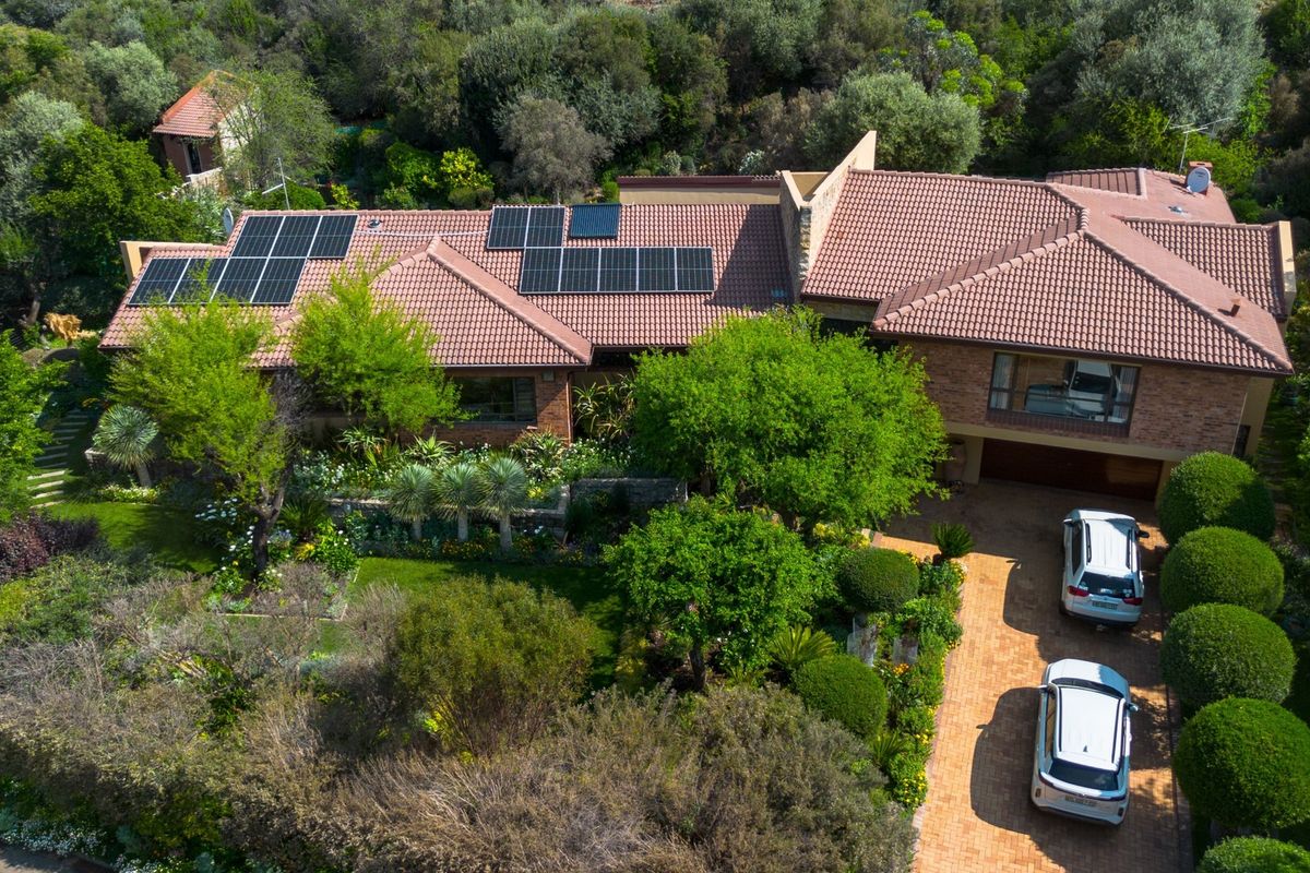 Aerial view of a spacious brick residence featuring a tiled roof with integrated solar panels, a paved driveway, and established landscaped gardens.