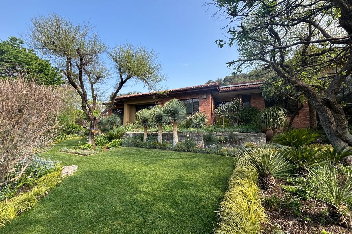 A well-maintained rear garden featuring a lush lawn, stone retaining wall, and established landscaping leading to a classic brick-faced house with a tiled roof.