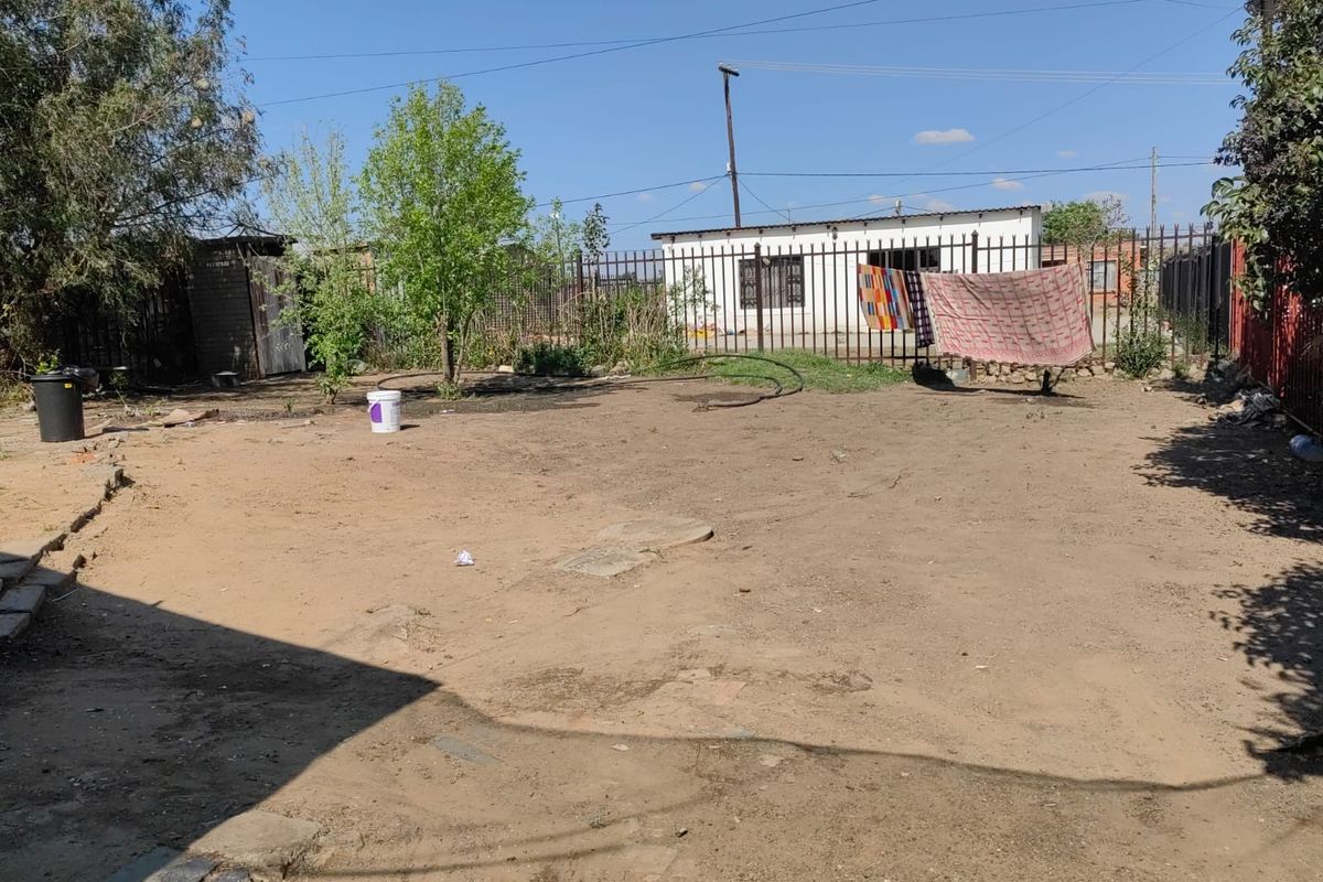 A spacious, unpaved rear yard featuring perimeter metal fencing and a small utility shed, offering significant potential for landscaping and outdoor development.