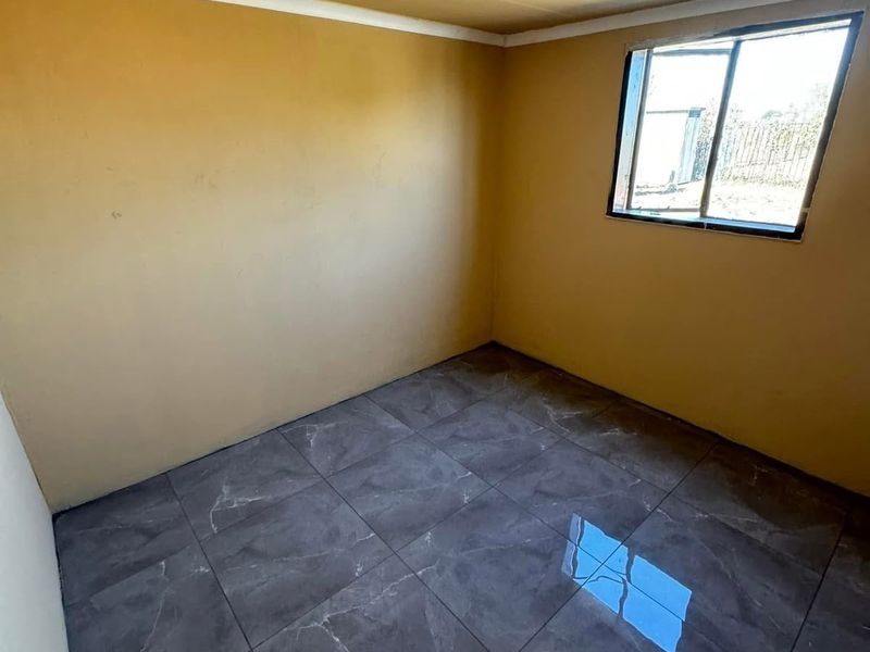 A vacant bedroom featuring dark grey tiled flooring, yellow painted walls, and a single sliding window.