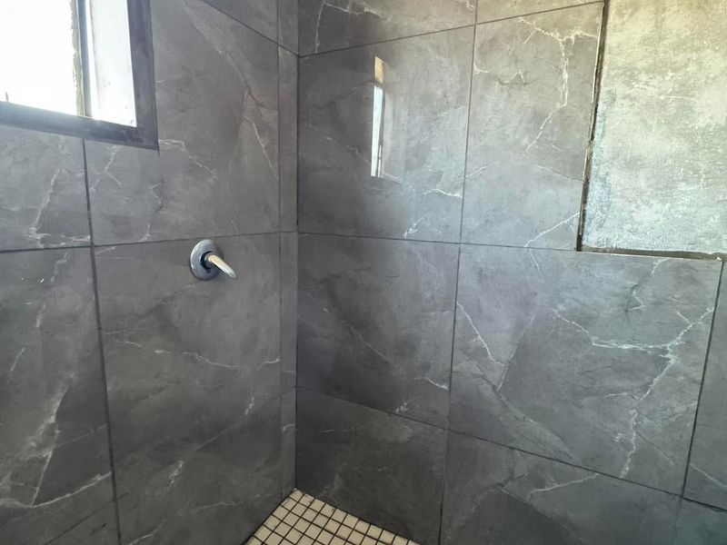 A shower enclosure featuring large-format grey marble-look wall tiles, a black rain shower head, and a mosaic-tiled shower floor.