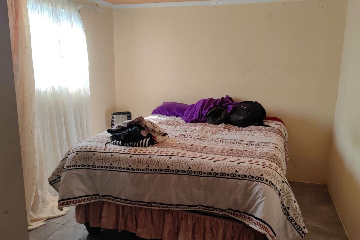 A simple bedroom featuring tiled flooring and natural light from a window with curtains.