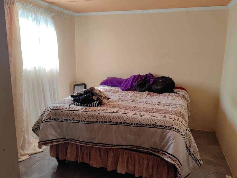 A simple bedroom featuring tiled flooring and natural light from a window with curtains.