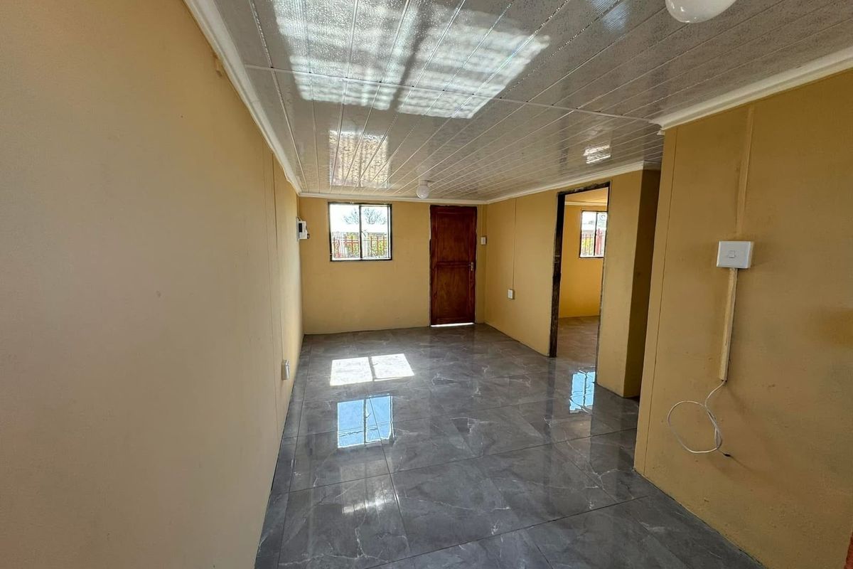 An empty living area featuring grey tiled flooring, PVC ceiling panels, and natural light through aluminium-framed windows.