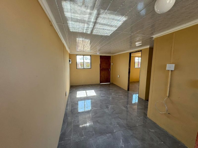An empty living area featuring grey tiled flooring, PVC ceiling panels, and natural light through aluminium-framed windows.