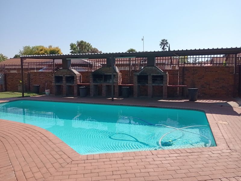 Outdoor pool area featuring a swimming pool, brick paving, and a covered communal braai facility with multiple built-in brick fireplaces.