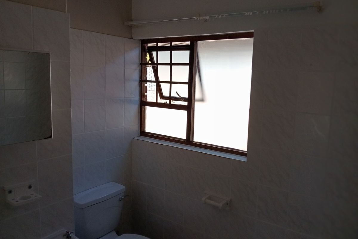 A functional bathroom featuring tiled walls, a standard toilet, and a window with security bars, offering a blank canvas for potential renovation.