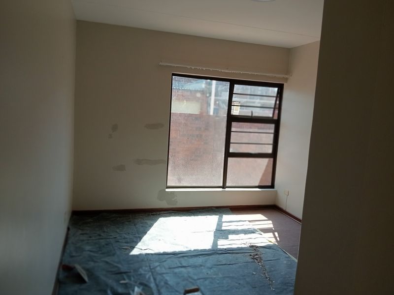 An empty bedroom featuring an aluminium window with security bars, requiring cosmetic wall repairs and new flooring to restore its appeal.