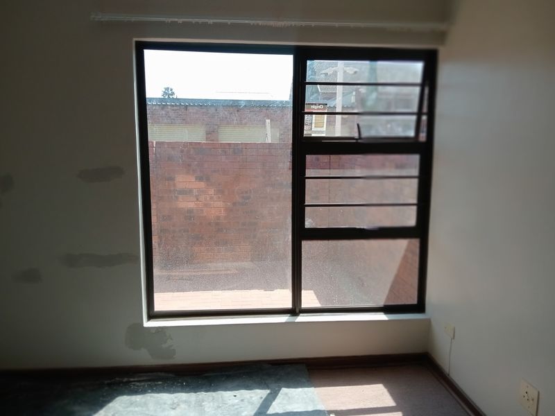 A vacant bedroom featuring an aluminium window with security bars, showing signs of wall surface damage requiring repair and repainting.