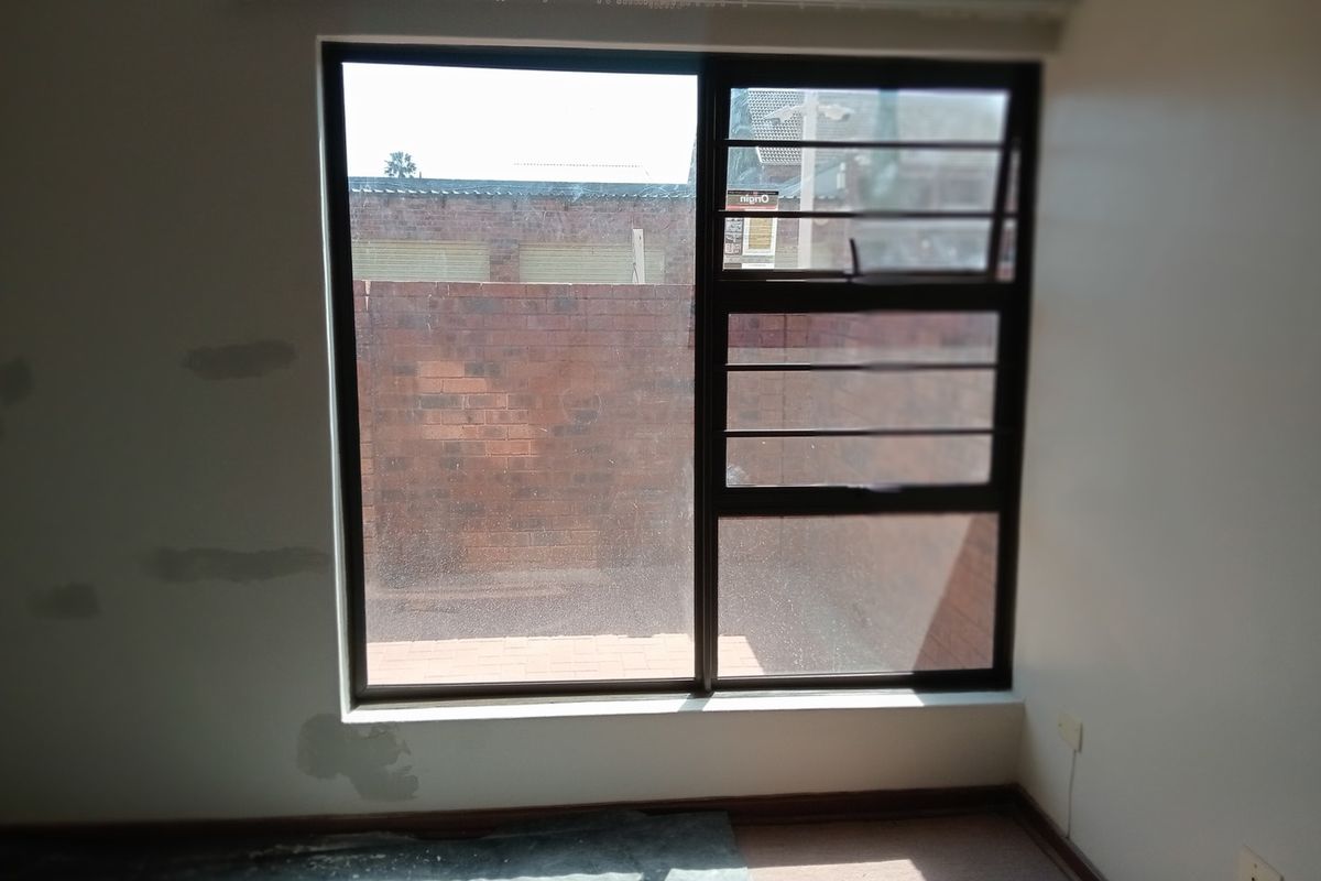 A vacant bedroom featuring an aluminium window with security bars, showing signs of wall surface damage requiring repair and repainting.