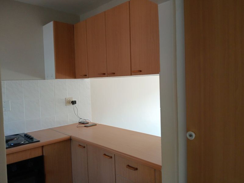 A functional kitchen area featuring light wood-look cabinetry, laminate countertops, and a built-in electric hob and oven with a tiled splashback.
