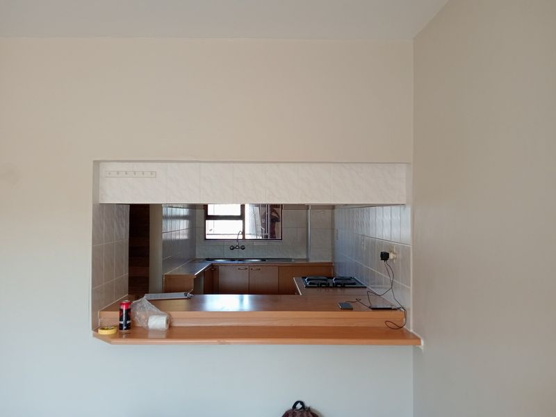 A functional kitchen featuring a breakfast bar pass-through, built-in cabinetry, gas hob, and stainless steel sink, offering a practical layout for daily use.