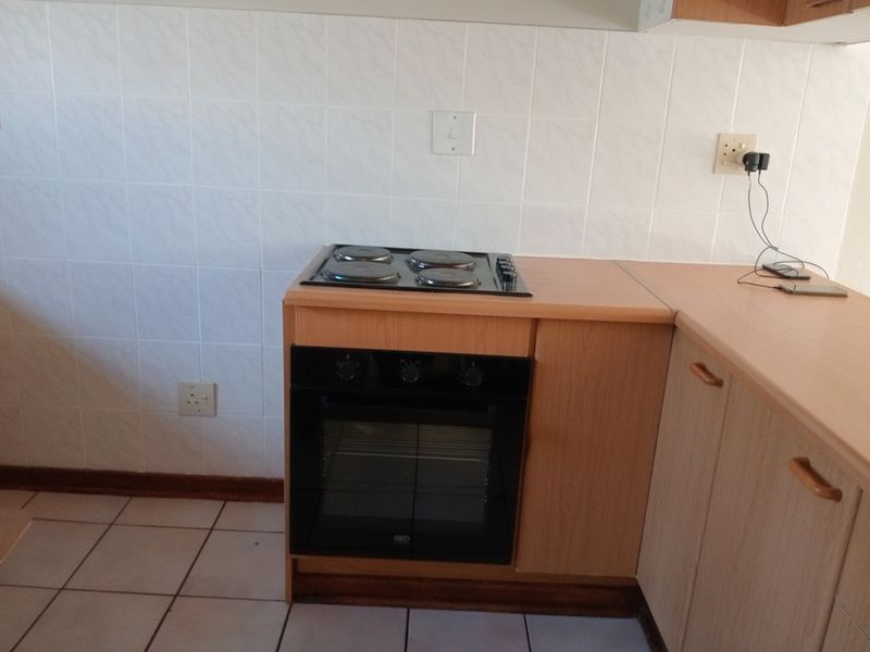 A functional kitchen area featuring a built-in oven, electric hob, laminate countertops, and tiled backsplash with neutral floor tiles.