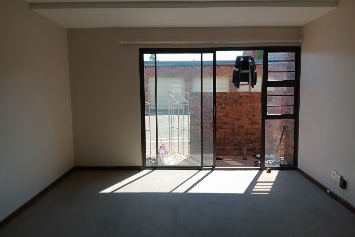 An empty living room featuring neutral walls, carpet flooring, and a large sliding glass door providing access to an outdoor area.