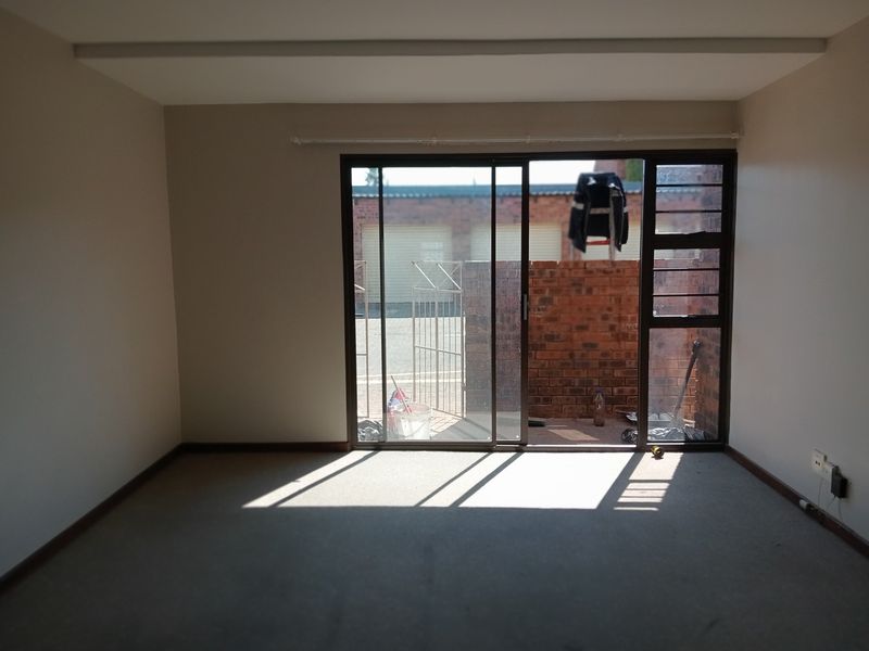 An empty living room featuring neutral walls, carpet flooring, and a large sliding glass door providing access to an outdoor area.