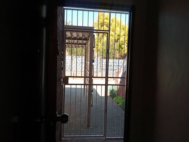 View from the entrance looking out through a security gate towards a paved courtyard and carport area.